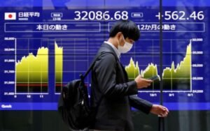 A man walks past an electric monitor displaying Japan's Nikkei share average and recent movements