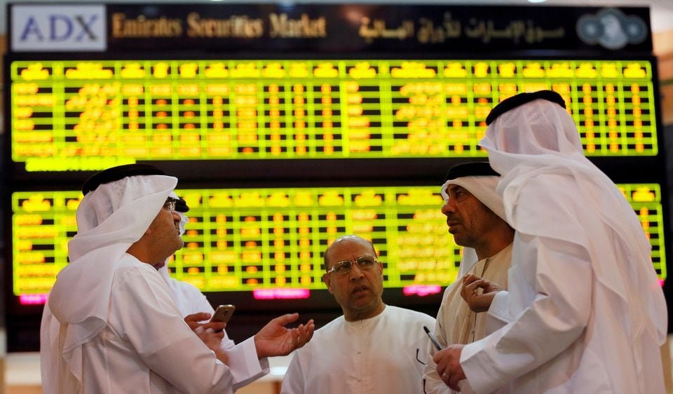 Investors speak in front of a screen displaying stock information at the Abu Dhabi Securities Exchange, United Arab Emirates June 25, 2014. REUTERS/Stringer/File Photo