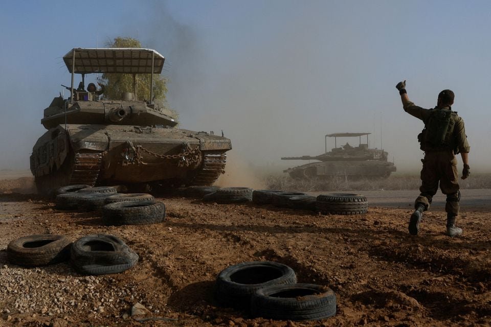 An Israeli soldier gestures towards a tank crew member as it crosses a road, as part of the convoy, amid the ongoing conflict between Israel and the Palestinian Islamist group Hamas, near Israel's border with southern Gaza, in Israel, December 4, 2023. REUTERS/Amir Cohen